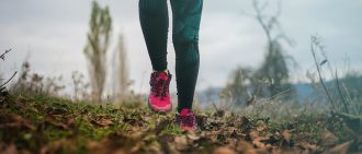 A cross country runner in pink shoes runs through leaves.